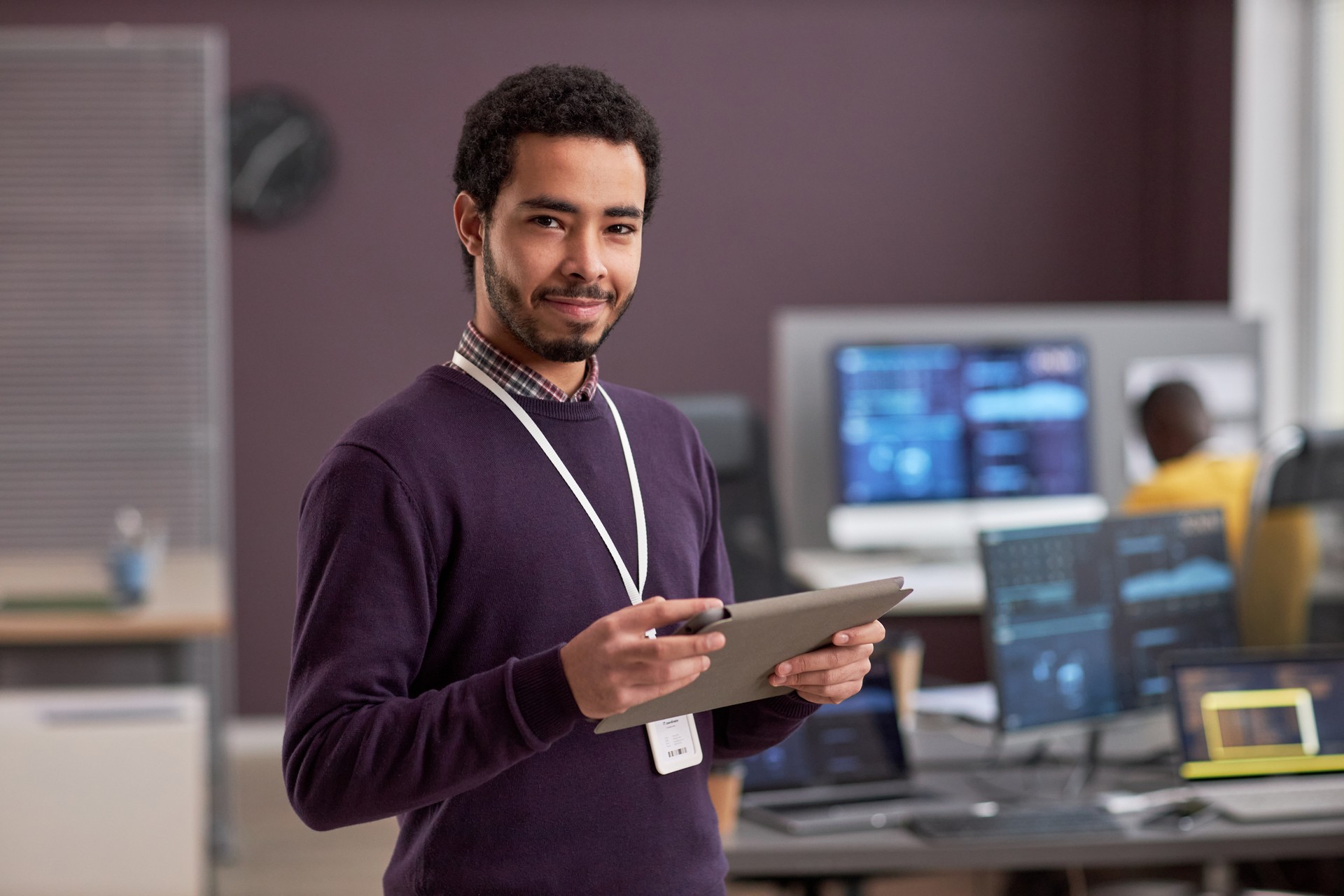 Ingeniero de software sonriente sosteniendo una tableta digital mientras está de pie en la oficina de tecnología